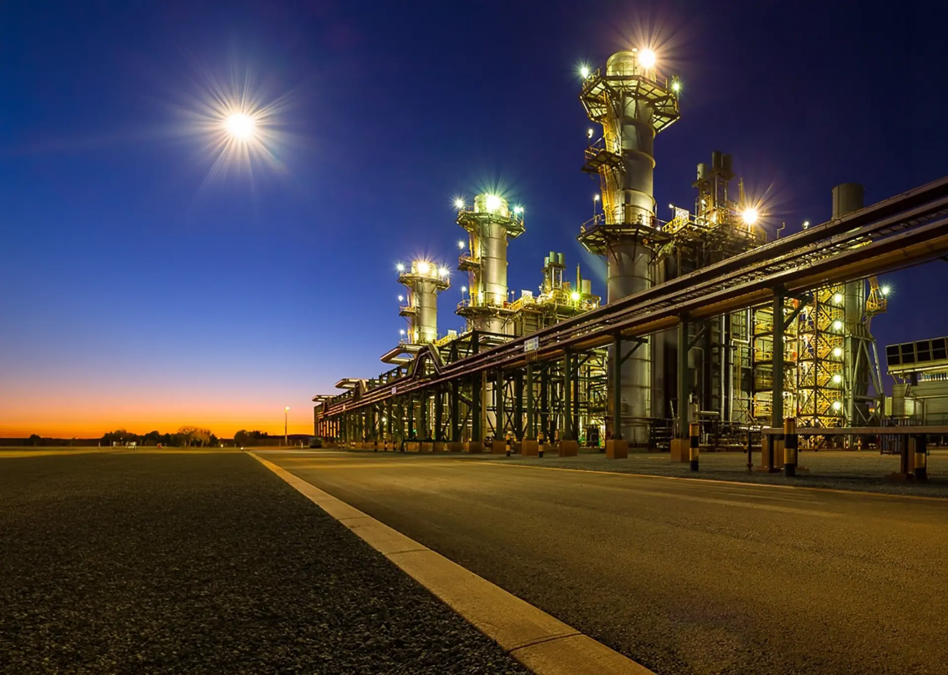 Gas-fired power station illuminated at dusk with pipe racks stretching to the horizon