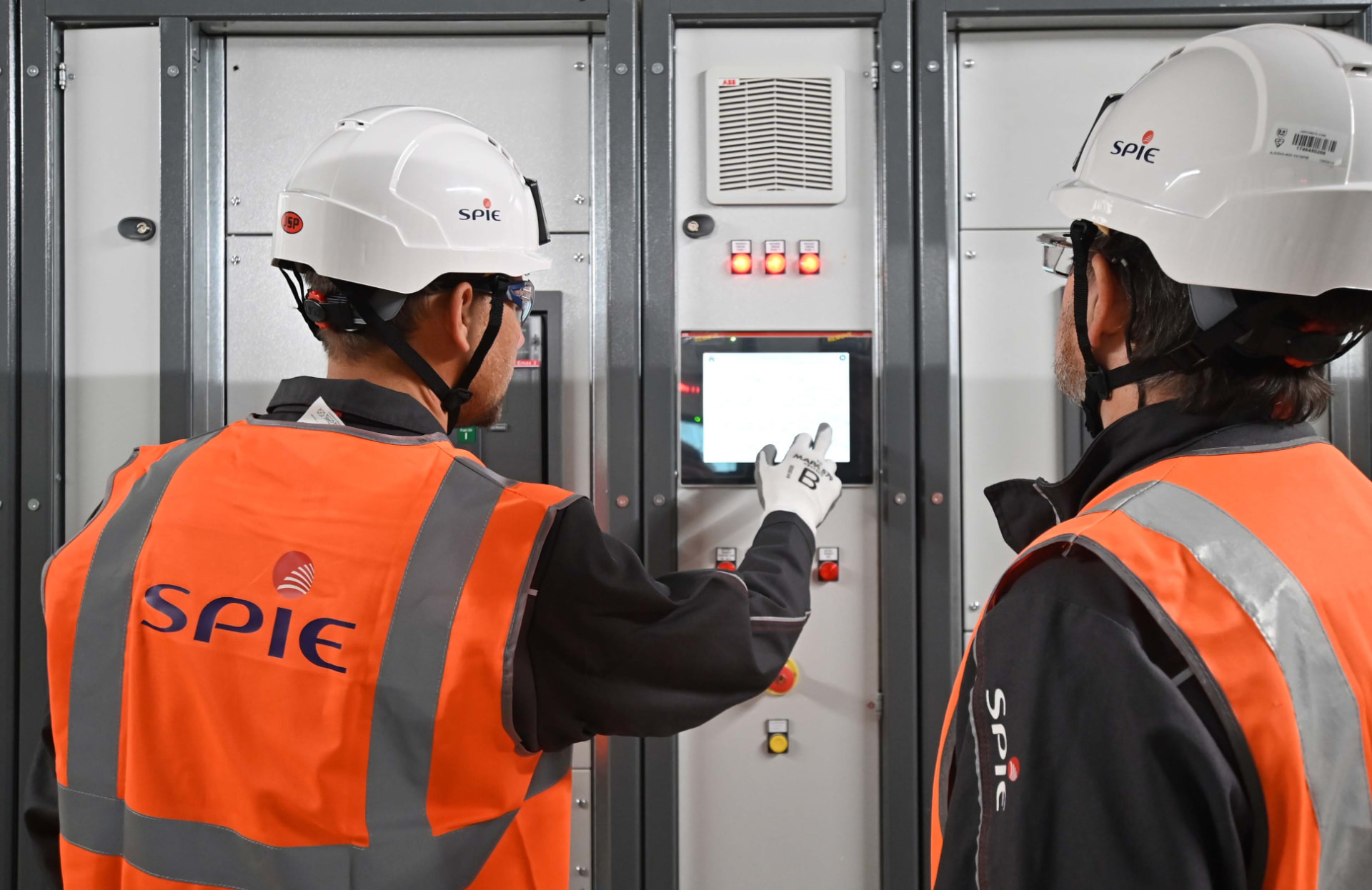 Two SPIE technicians in high-vis operating a control panel inside a switchroom