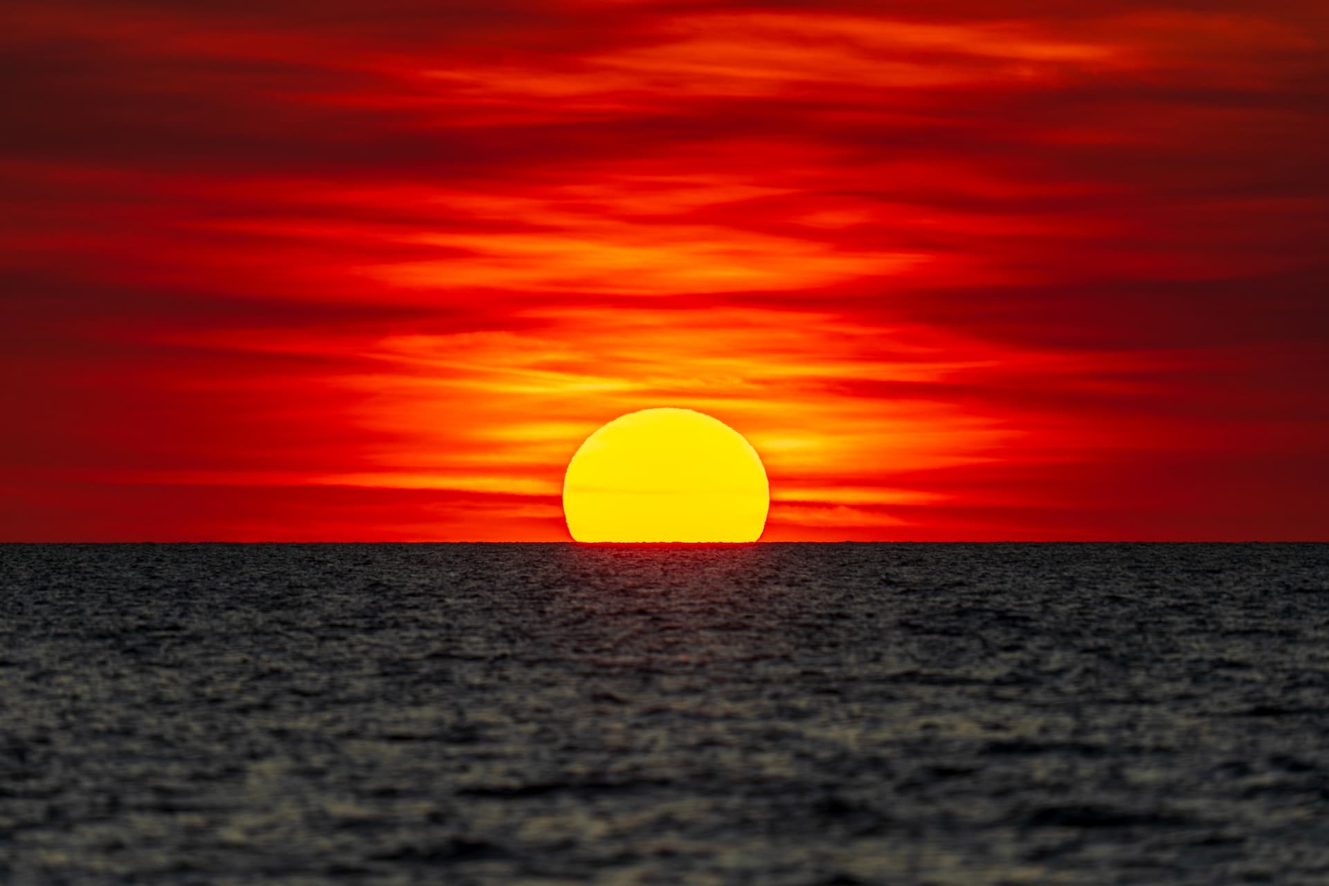 Sun setting over the ocean horizon in a deep red sky