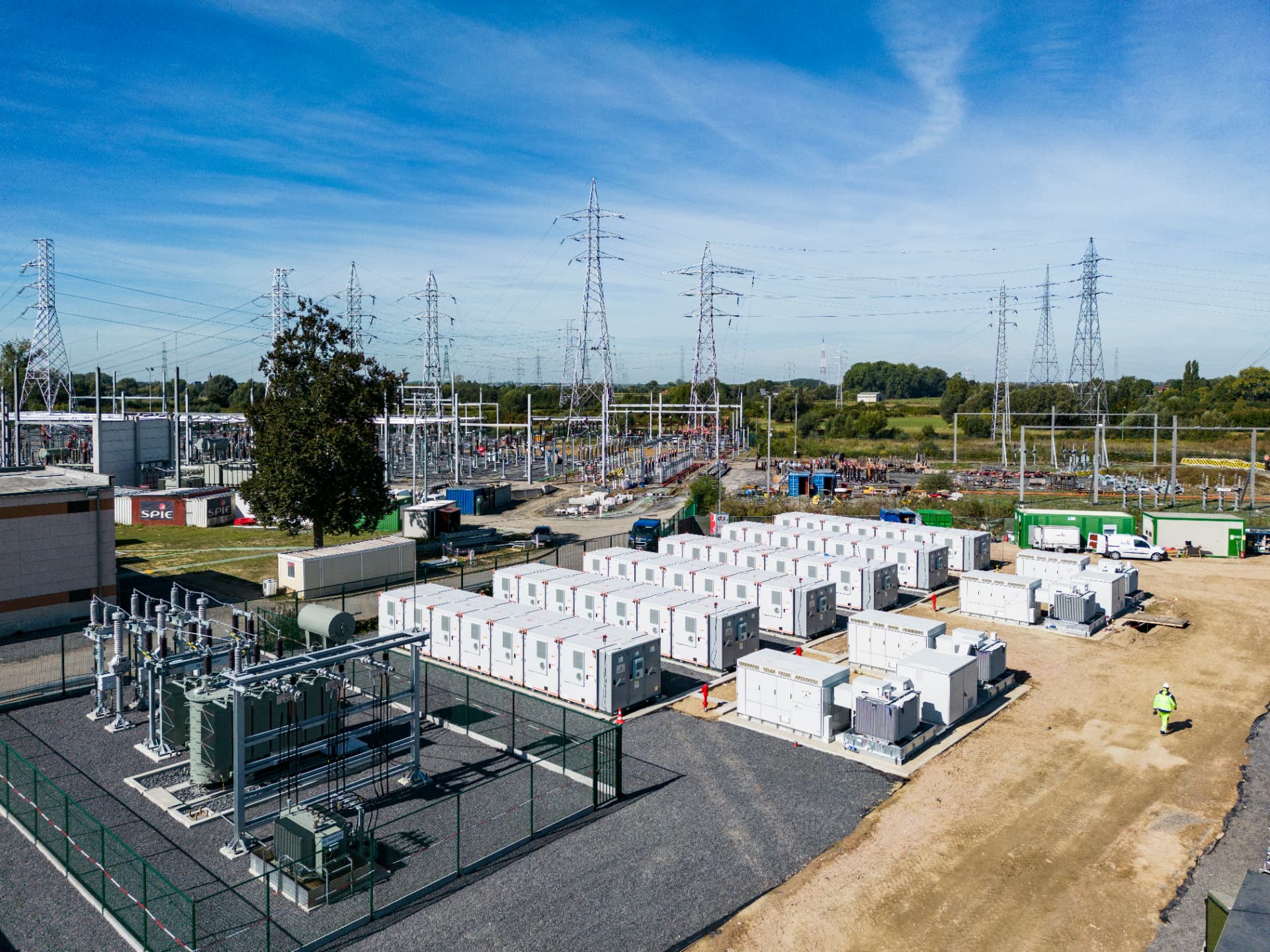 Aerial view of a grid-scale battery storage park beside a high-voltage substation