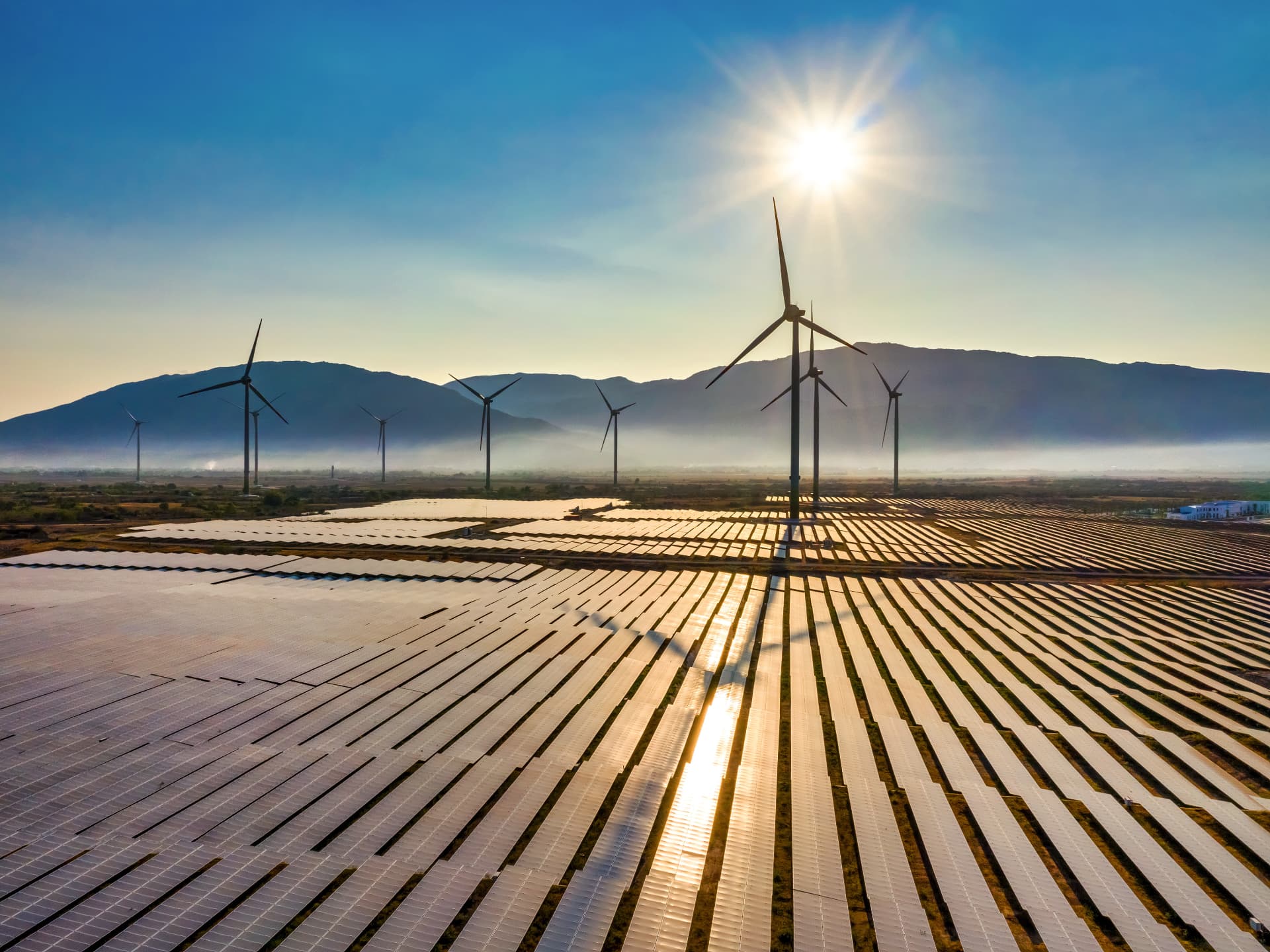 Wind turbines and solar panels at sunrise in front of a mountain range